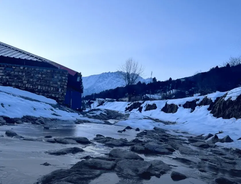 Meltwater running down a village track between banks of dirty snow at dusk