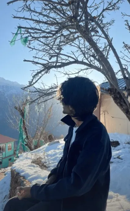 Sitting on a low wall under a bare tree, looking out over a snowbound village at first light