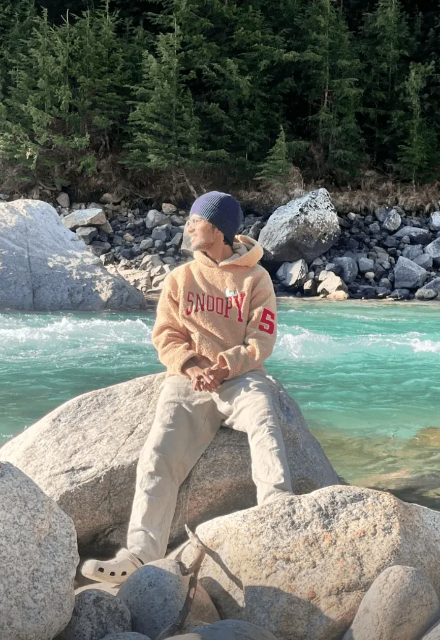 Sitting on a granite boulder beside a turquoise glacial river, pines on the far bank