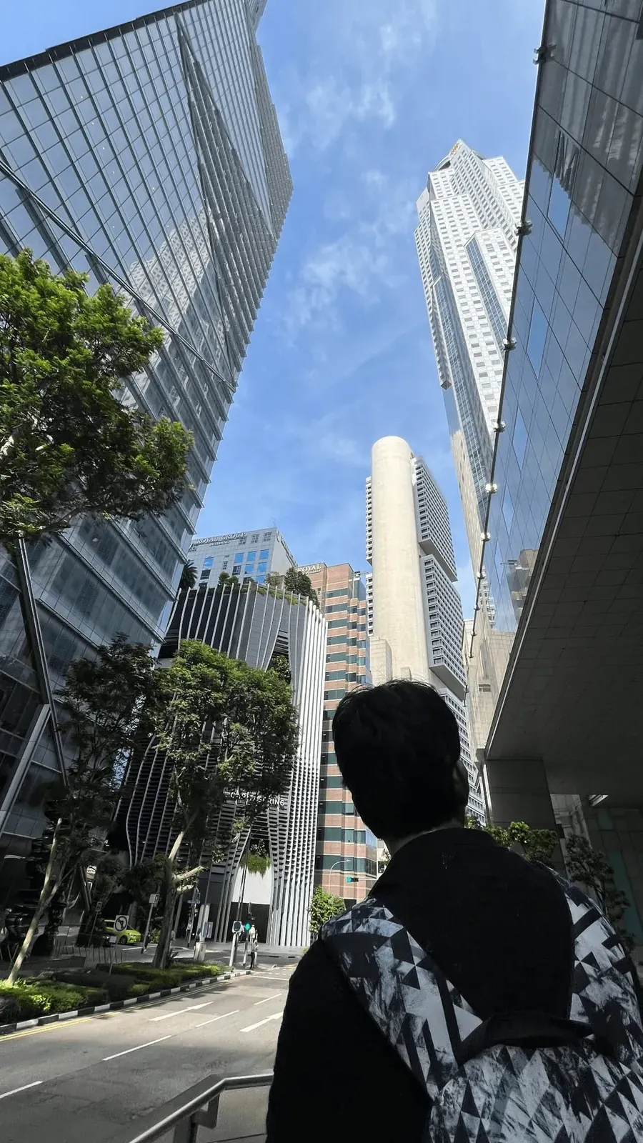 Looking up between glass towers in a business district, one figure in the foreground